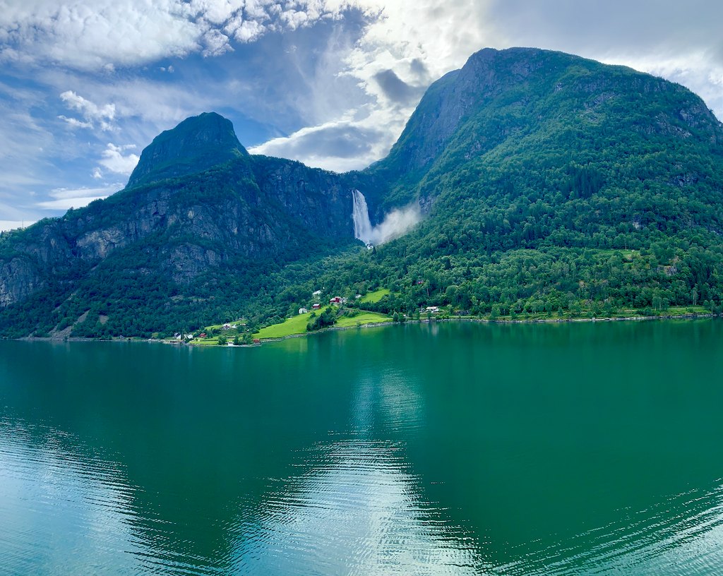 A waterfall between green mountains above calm, reflective water.
